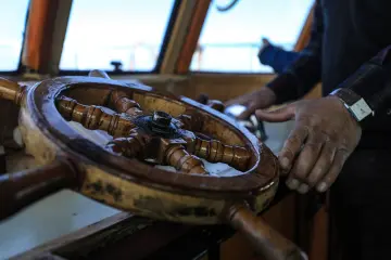 Ahşap gemi dümeni üzerindeki kaptan elleri, denizcilik ve güvenli seyri simgeleyen etkileyici bir detay sunuyor.