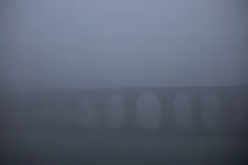 Diyarbakır On Gözlü Köprü'nün yoğun sis altında Dicle Nehri üzerindeki silueti ve suya yansıyan görünümü.