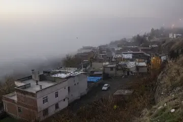 Diyarbakır'da yoğun sis altında kalan yamaç yerleşimi, evler, ağaçlar ve akşam ışıklarıyla etkileyici kent manzarası.