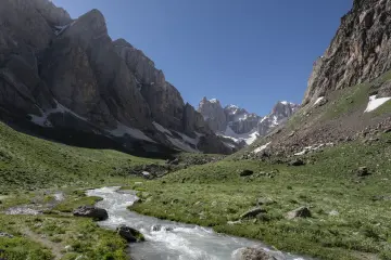 Hakkâri Cennet-Cehennem Vadisi'nde sarp kayalıklar, kar kalıntıları, yeşil yamaçlar ve berrak dağ deresi.