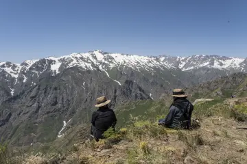 Hakkâri Cilo-Sat Dağları'nda karlı zirveleri izleyen iki kişi ve etkileyici yüksek dağ manzarası.