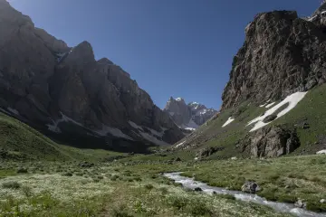 Hakkâri Cilo Dağları'nda sarp kayalıklarla çevrili karlı vadi, yeşil yamaçlar ve akarsu manzarası.