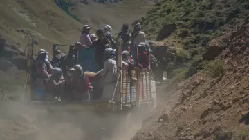 Hakkari yaylasında kamyonet kasasında yolculuk yapan insanlar ve tozlu dağ yolu