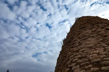 Şanlıurfa Harran Antik Kenti'ndeki tarihi taş duvarı ve etkileyici bulutlu gökyüzünü gösteren editoryal fotoğraf.