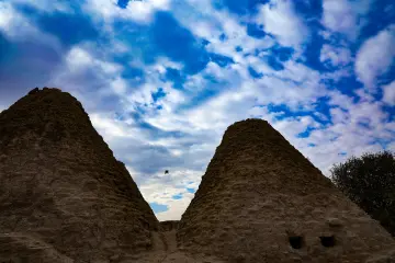 Harran Kümbet Evleri'nin konik kubbeleri ve bulutlu gökyüzü altında geleneksel mimari görünümü.