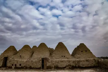 Harran'ın konik kubbeli kerpiç evleri ve etkileyici bulutlu gökyüzünü yansıtan tarihi yerleşim görünümü.