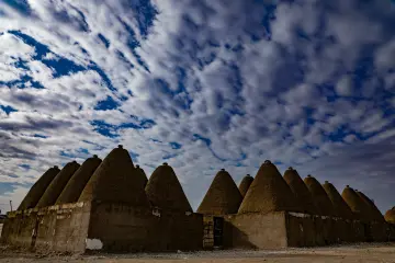 Harran'ın konik kubbeli kerpiç evleri ve etkileyici bulutlu gökyüzünü yansıtan tarihi yerleşim manzarası.