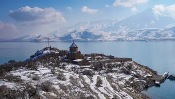 Akdamar Adası ve Akdamar Kilisesi'nin Van Gölü üzerindeki kış manzarasını gösteren panoramik hava fotoğrafı.