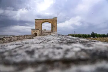 Dramatik bulutlar altında Malabadi Köprüsü'nün taş dokusunu ve tarihi kemerini öne çıkaran etkileyici perspektif.