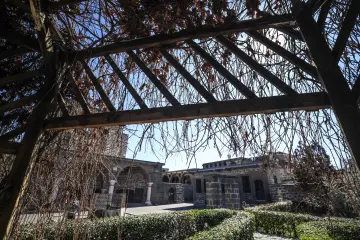 Meryem Ana Süryani Kadim Kilisesi avlusunda ahşap pergola, sarmaşıklar ve tarihi taş mimari.