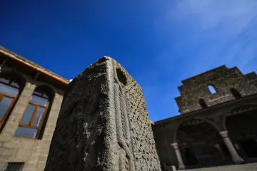 Meryem Ana Süryani Kadim Kilisesi avlusunda tarihi taş detay, kemerli mimari ve mavi gökyüzü.