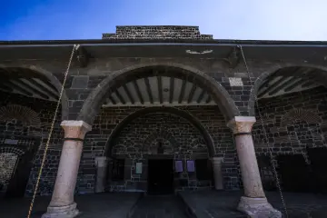 Meryem Ana Süryani Kadim Kilisesi'nin bazalt taş duvarlı, kemerli ve sütunlu tarihi avlu görünümü.