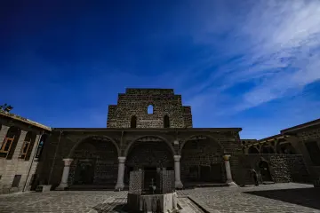 Meryem Ana Süryani Kadim Kilisesi'nin bazalt taş duvarlı, kemerli ve sütunlu tarihi avlu görünümü.