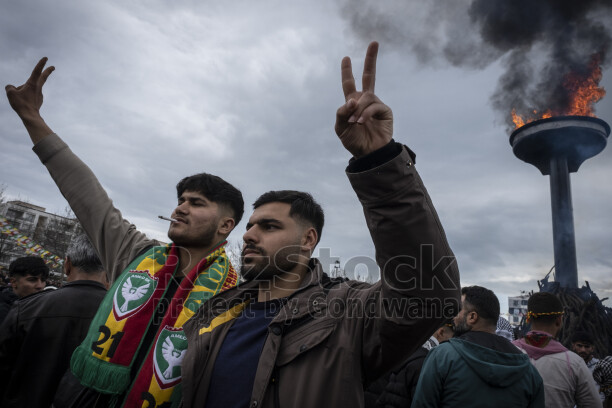 21 Mart 2025 Diyarbakır Amed Newrozunda Amedspor atkılı katılımcılar zafer işareti yaparken Newroz ateşi yanıyor.