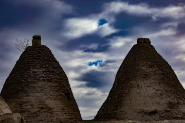 Şanlıurfa Harran kümbet evleri, dramatik gökyüzü altında tarihi kerpiç mimari ve Mezopotamya kültürünü yansıtan fotoğraf.