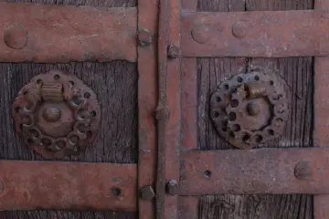 Tarihi ahşap kapıda dekoratif metal kuşaklar, çiviler ve geleneksel el işçiliği detayları.