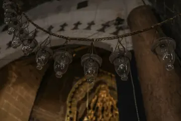 Tarihi kilisenin iç mekanında zincirlerle asılmış cam aydınlatma elemanları ve taş mimari detaylar.