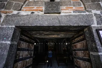 Tarihi kilisenin ahşap ve demir detaylı giriş kapısı, taş mimari ve dekoratif duvar motifi.