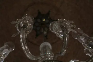 Tarihi yapının iç mekanında bulunan cam avizenin kavisli kolları ve dekoratif cam detaylarının yakın plan görünümü.