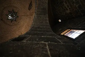 Tarihi yapının tuğla kubbesi, taş duvarları, küçük pencereleri ve geometrik aydınlatma detayı.