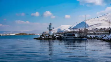 Van Gölü kıyısındaki deniz feneri, iskele ve karla kaplı dağların buluştuğu etkileyici kış manzarası.