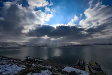 Van Gölü'nde bulutların arasından süzülen güneş ışınları, karlı dağlar ve teknelerle büyüleyici kış manzarası sunuyor.