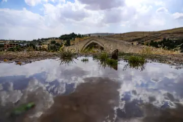 Yağmur sonrası oluşan yansımada Malabadi Köprüsü ve bulutların buluştuğu etkileyici Diyarbakır manzarası.
