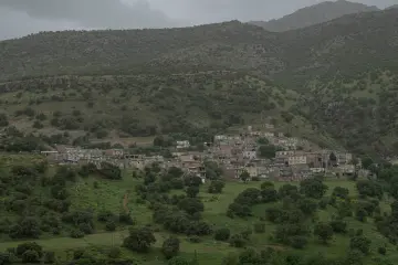 Yeşil dağlarla çevrili vadide yamaç boyunca uzanan yerleşim ve doğal peyzaj manzarası.