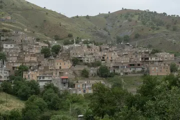 Yeşil dağ yamacına yayılan geleneksel yerleşim, taş yapılar ve çevresindeki doğal peyzaj manzarası.